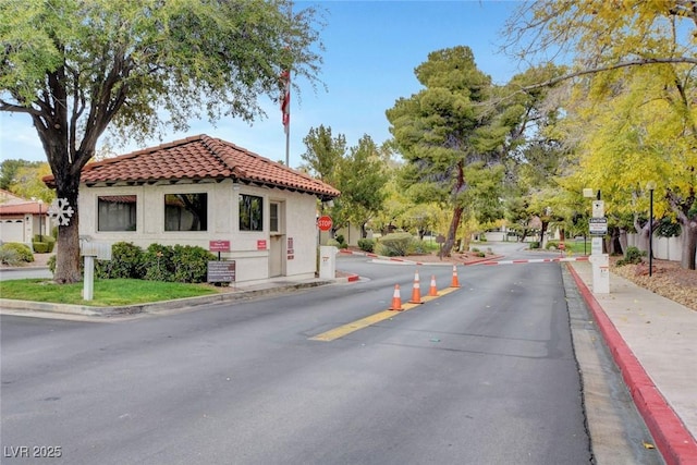 view of asphalt street featuring curbs, traffic signs, sidewalks, and a gated entry