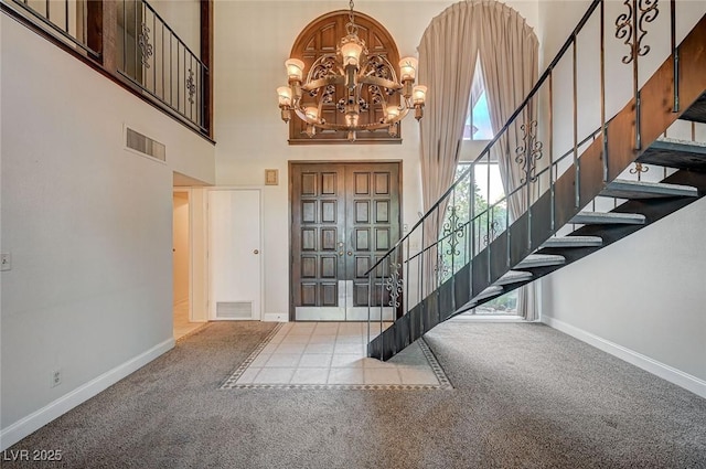 entrance foyer with a towering ceiling, a chandelier, stairs, baseboards, and carpet