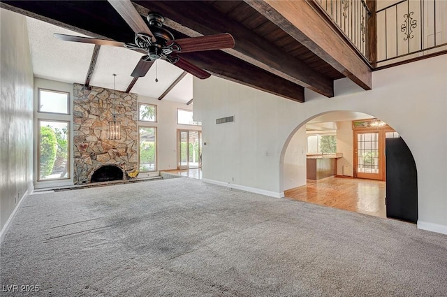 unfurnished living room with carpet floors, baseboards, a ceiling fan, a fireplace, and beamed ceiling