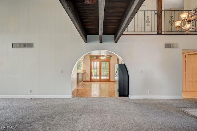 carpeted foyer featuring arched walkways, beamed ceiling, baseboards, and wood ceiling