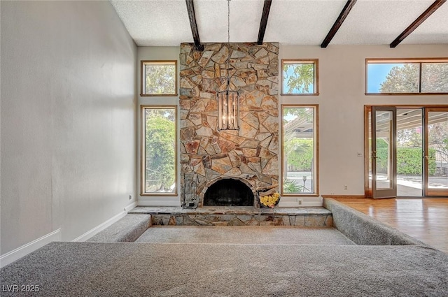 unfurnished living room with beam ceiling, carpet flooring, baseboards, a stone fireplace, and high vaulted ceiling