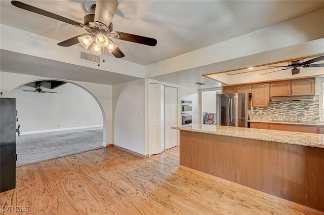 kitchen featuring freestanding refrigerator, ceiling fan, light wood-style floors, light stone countertops, and baseboards