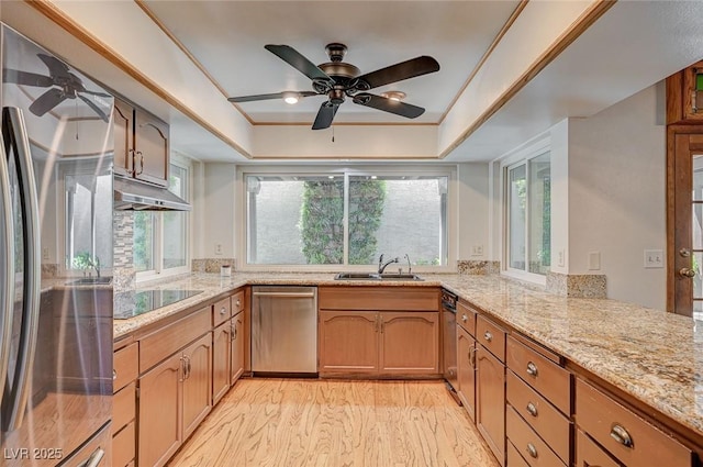 kitchen featuring appliances with stainless steel finishes, a ceiling fan, a sink, under cabinet range hood, and a tray ceiling