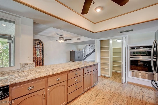 kitchen with a ceiling fan, light wood-type flooring, light stone countertops, and a peninsula