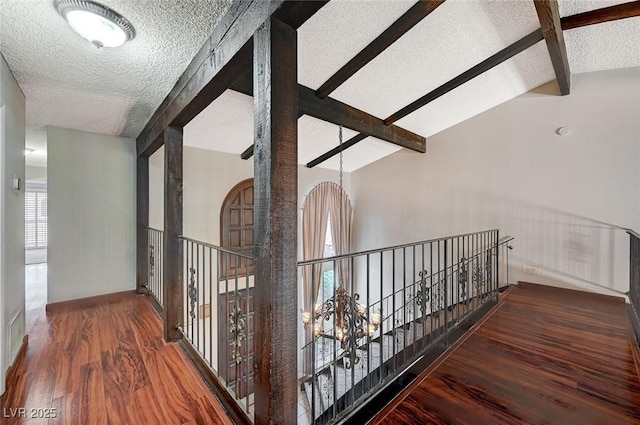 hall with a textured ceiling, wood finished floors, and an upstairs landing