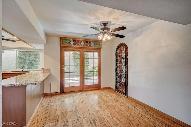 doorway featuring light wood-style flooring, baseboards, a ceiling fan, a sink, and french doors