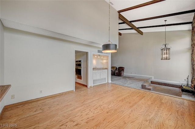 unfurnished living room with wood finished floors, beam ceiling, a chandelier, and baseboards