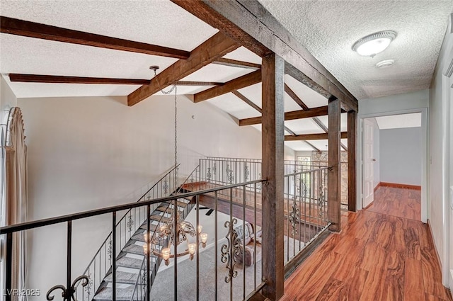 hallway with a textured ceiling, wood finished floors, and an upstairs landing