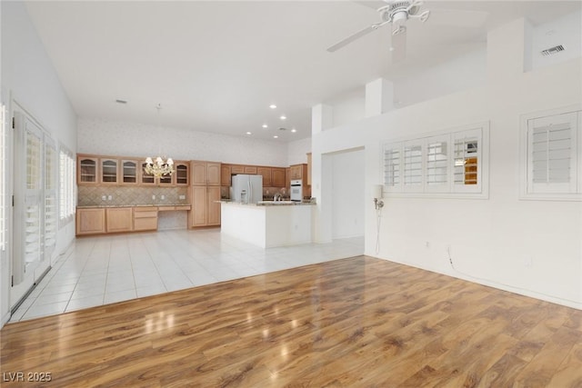 unfurnished living room featuring light wood-style floors, ceiling fan with notable chandelier, recessed lighting, a towering ceiling, and visible vents