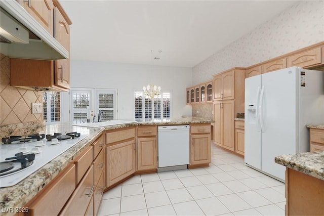 kitchen with white appliances, light brown cabinetry, under cabinet range hood, and wallpapered walls