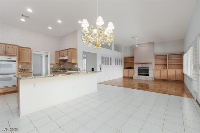 kitchen with visible vents, a glass covered fireplace, double oven, ceiling fan with notable chandelier, and backsplash