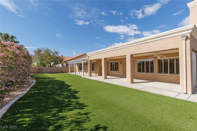 rear view of house with ceiling fan, stucco siding, a fenced backyard, a patio area, and a lawn