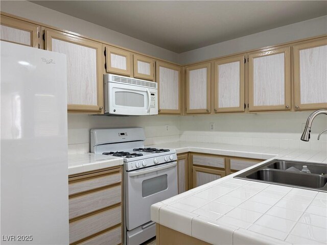 kitchen featuring tile counters, a sink, light brown cabinets, and white appliances