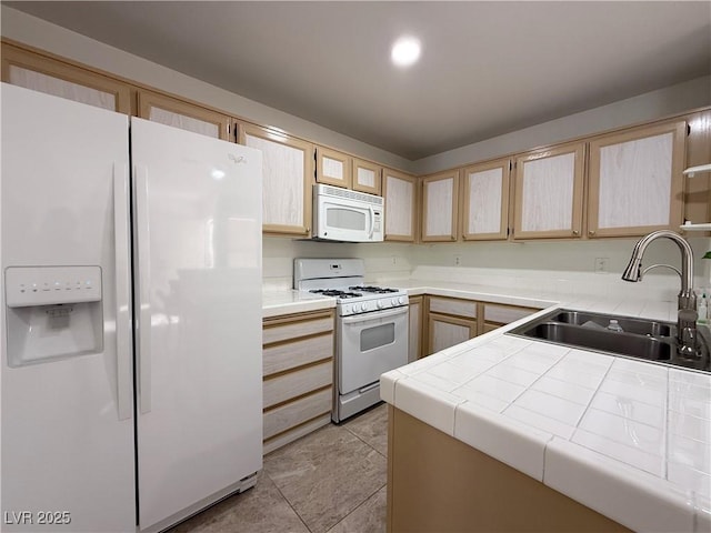 kitchen with a sink, light brown cabinets, tile countertops, and white appliances
