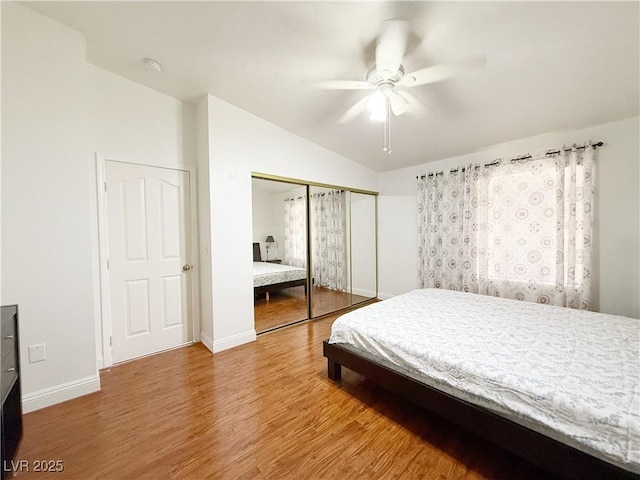 bedroom with a ceiling fan, baseboards, wood finished floors, lofted ceiling, and a closet