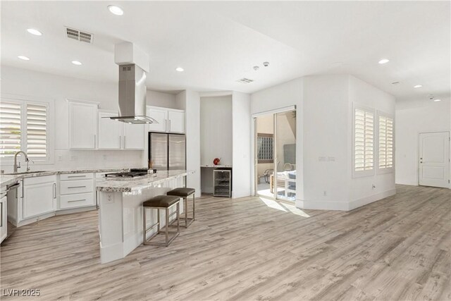 kitchen featuring island range hood, appliances with stainless steel finishes, light wood finished floors, a sink, and visible vents