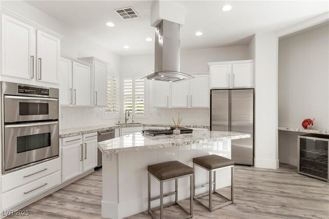 kitchen featuring a sink, island range hood, visible vents, stainless steel appliances, and a kitchen island
