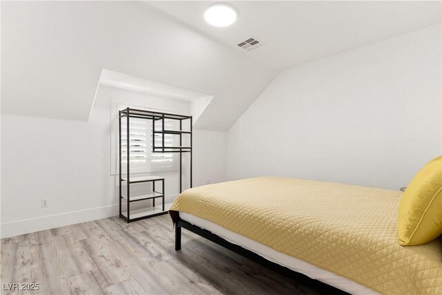 bedroom with lofted ceiling, wood finished floors, visible vents, and baseboards