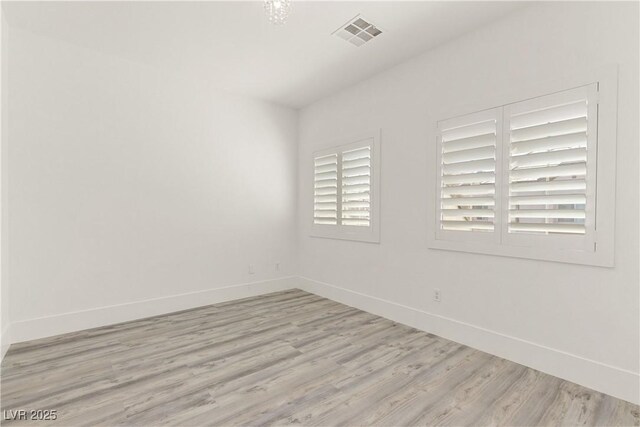 spare room featuring light wood finished floors, visible vents, and baseboards