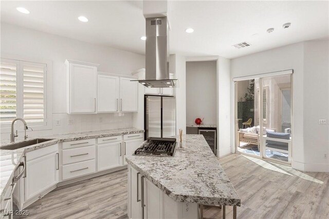 kitchen featuring a sink, stainless steel appliances, visible vents, island range hood, and beverage cooler