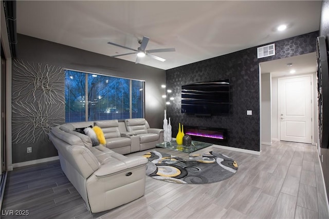 living room with visible vents, an accent wall, wallpapered walls, a ceiling fan, and wood finished floors