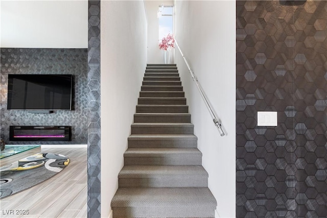 staircase featuring wood finished floors and a glass covered fireplace