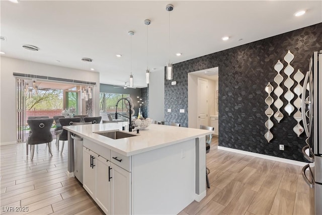 kitchen featuring stainless steel appliances, a sink, baseboards, an accent wall, and wallpapered walls