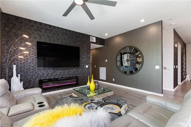 living room with baseboards, visible vents, an accent wall, a ceiling fan, and wood finished floors