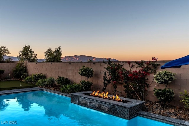 5852 Ireland Ridge Ct, Las Vegas, NV 89149 - pool at dusk with an outdoor fire pit, a putting area, and a fenced backyard