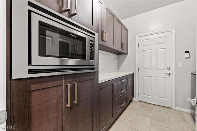 5852 Ireland Ridge Ct, Las Vegas, NV 89149 - kitchen featuring stainless steel microwave, dark brown cabinetry, decorative backsplash, baseboards, and light tile patterned flooring