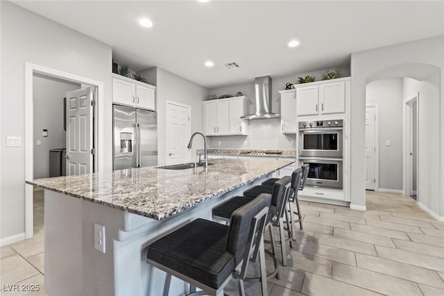 5852 Ireland Ridge Ct, Las Vegas, NV 89149 - kitchen with appliances with stainless steel finishes, wall chimney range hood, a sink, a kitchen bar, and white cabinetry