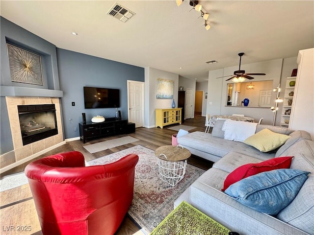 living area featuring a tiled fireplace, baseboards, visible vents, wood finished floors, and ceiling fan