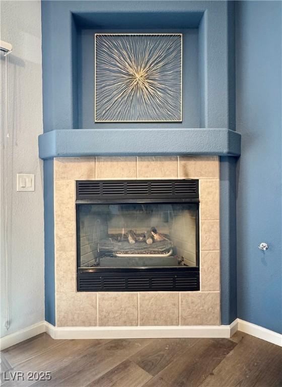 details featuring a tile fireplace, baseboards, and wood finished floors