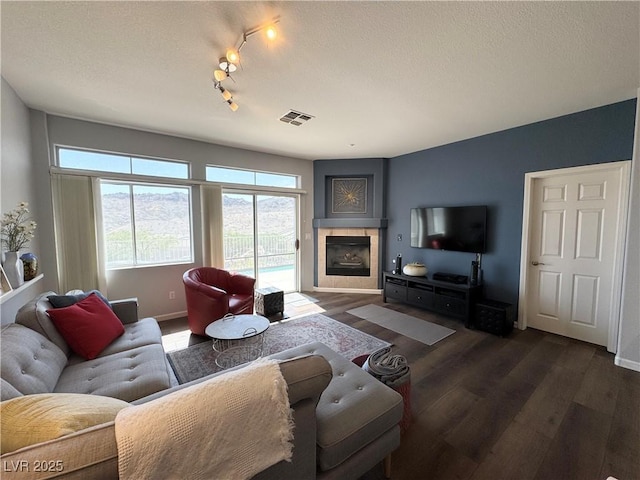 living area with dark wood-style flooring, a tiled fireplace, baseboards, visible vents, and track lighting