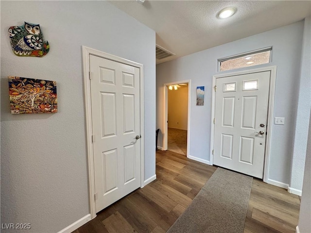foyer with dark wood-type flooring, a textured ceiling, visible vents, and baseboards