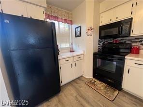 kitchen with light wood-type flooring, light countertops, white cabinets, and black appliances