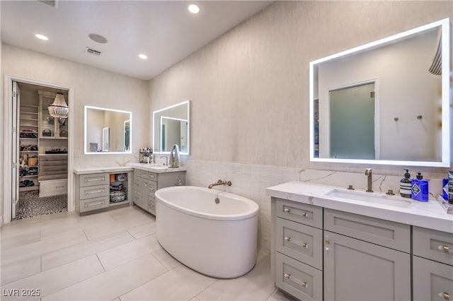 bathroom with visible vents, a sink, tile walls, two vanities, and a freestanding tub