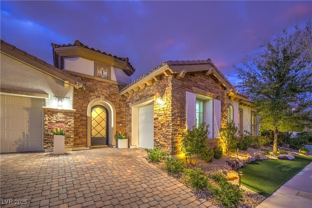 view of front of property featuring an attached garage, stone siding, a tiled roof, and stucco siding