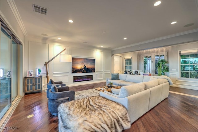 living area with wood finished floors, a decorative wall, ornamental molding, and visible vents