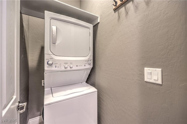 clothes washing area featuring a textured wall, stacked washing maching and dryer, and laundry area