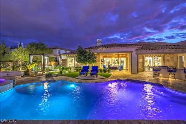 pool at dusk with an outdoor pool and a patio