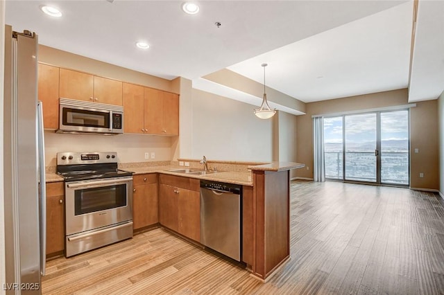 kitchen with a sink, light wood finished floors, stainless steel appliances, recessed lighting, and a peninsula