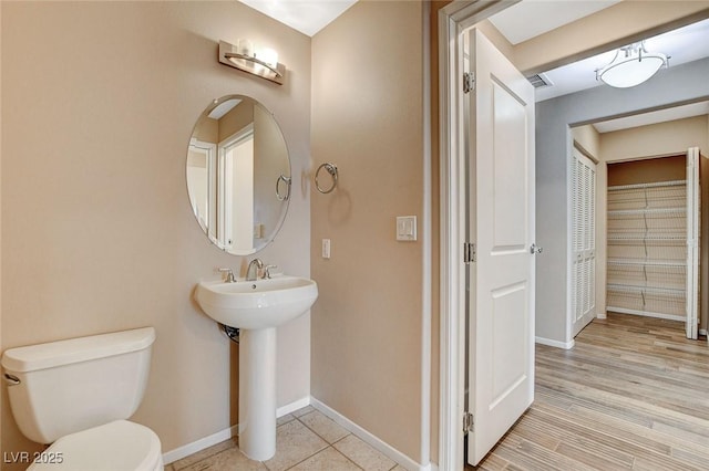 half bathroom with baseboards, a sink, visible vents, and toilet