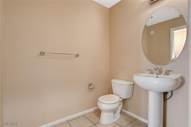 half bath with a sink, baseboards, tile patterned flooring, and toilet
