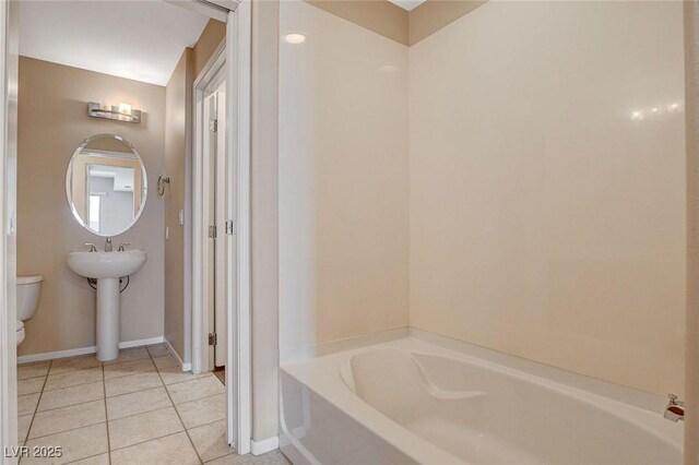 bathroom featuring toilet, tile patterned floors, baseboards, and a bath