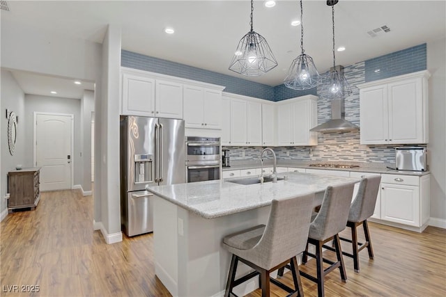 kitchen with a sink, light wood finished floors, white cabinets, baseboards, and appliances with stainless steel finishes