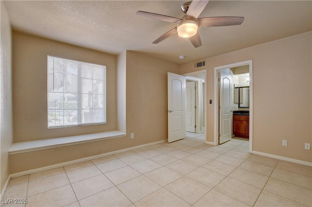 unfurnished bedroom featuring light tile patterned floors, a textured ceiling, visible vents, baseboards, and a ceiling fan