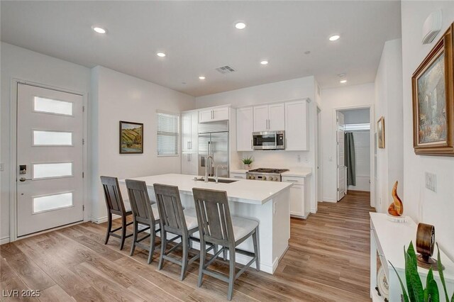 897 Woodburn Ln, Las Vegas, NV 89138 - kitchen with appliances with stainless steel finishes, a kitchen island with sink, a breakfast bar, white cabinets, and light wood-type flooring