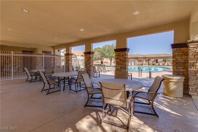 view of patio with a community pool, outdoor dining area, and fence