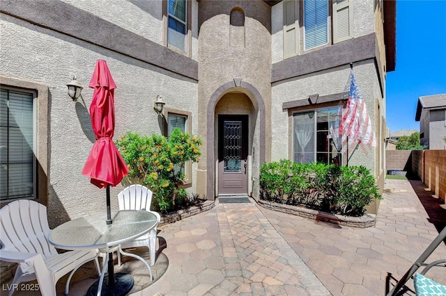 doorway to property featuring a patio area, fence, outdoor dining area, and stucco siding